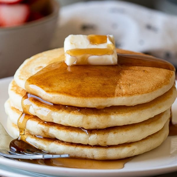 Stack of golden pancakes with melting butter and maple syrup dripping down the sides.