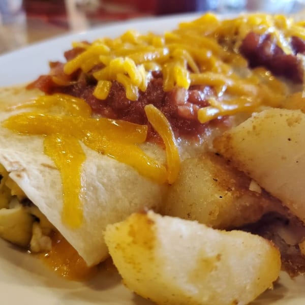 A breakfast burrito topped with cheese and salsa, served with crispy hash browns.
